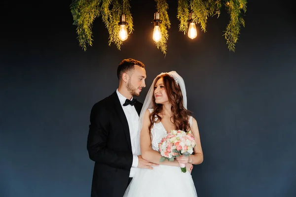 The first meeting of the groom in a black suit and the bride in a white wedding dress with a bouquet in the interior of a photo studio on a white and black background