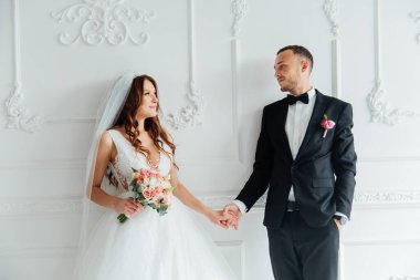 Damadın siyah takım elbiseli ilk buluşması ve beyaz gelinlikli gelinin beyaz ve siyah arka planda bir fotoğraf stüdyosunun içinde bir buket olması.