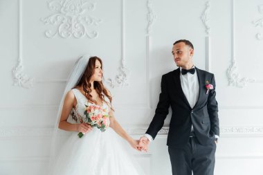 Damadın siyah takım elbiseli ilk buluşması ve beyaz gelinlikli gelinin beyaz ve siyah arka planda bir fotoğraf stüdyosunun içinde bir buket olması.