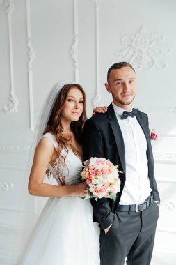 Damadın siyah takım elbiseli ilk buluşması ve beyaz gelinlikli gelinin beyaz ve siyah arka planda bir fotoğraf stüdyosunun içinde bir buket olması.