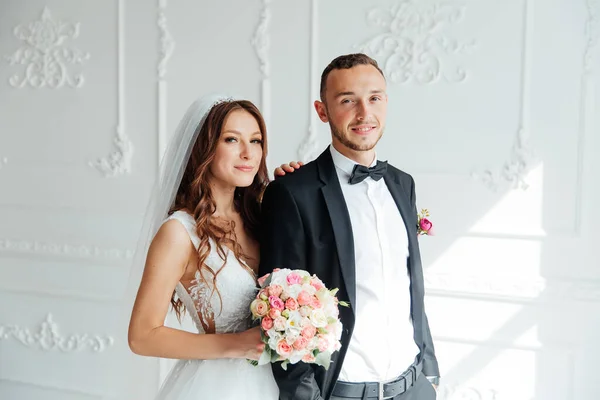 The first meeting of the groom in a black suit and the bride in a white wedding dress with a bouquet in the interior of a photo studio on a white and black background