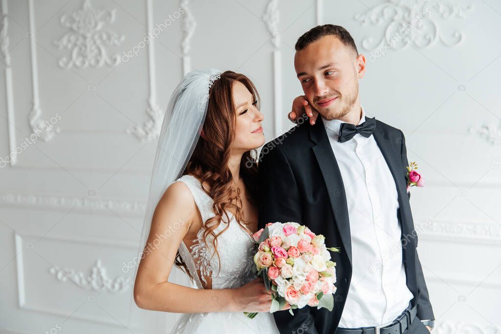 The first meeting of the groom in a black suit and the bride in a white wedding dress with a bouquet in the interior of a photo studio on a white and black background