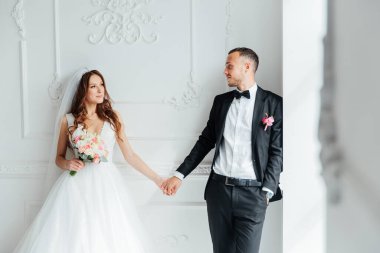 Damadın siyah takım elbiseli ilk buluşması ve beyaz gelinlikli gelinin beyaz ve siyah arka planda bir fotoğraf stüdyosunun içinde bir buket olması.