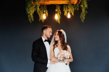 Damadın siyah takım elbiseli ilk buluşması ve beyaz gelinlikli gelinin beyaz ve siyah arka planda bir fotoğraf stüdyosunun içinde bir buket olması.