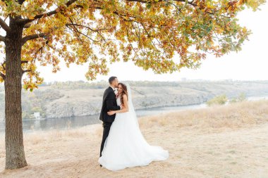 Güzel, lüks bir çiftin düğün yürüyüşü, gelin beyaz bir elbise ve bir buket ve damat açık havada siyah bir takım elbise içinde