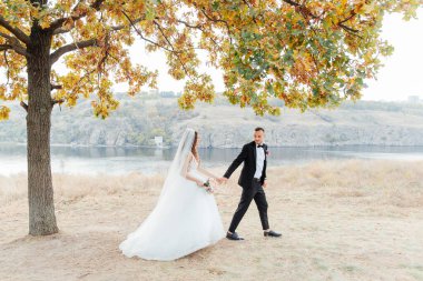 Güzel, lüks bir çiftin düğün yürüyüşü, gelin beyaz bir elbise ve bir buket ve damat açık havada siyah bir takım elbise içinde