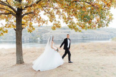 Güzel, lüks bir çiftin düğün yürüyüşü, gelin beyaz bir elbise ve bir buket ve damat açık havada siyah bir takım elbise içinde