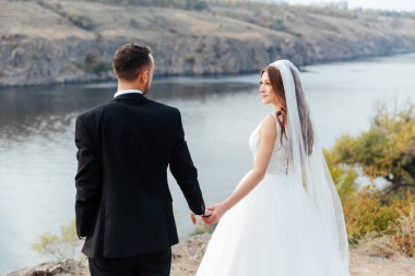 Güzel, lüks bir çiftin düğün yürüyüşü, gelin beyaz bir elbise ve bir buket ve damat açık havada siyah bir takım elbise içinde