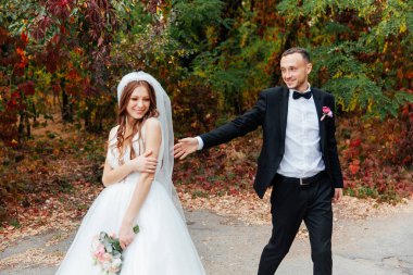 Güzel, lüks bir çiftin düğün yürüyüşü, gelin beyaz bir elbise ve bir buket ve damat açık havada siyah bir takım elbise içinde