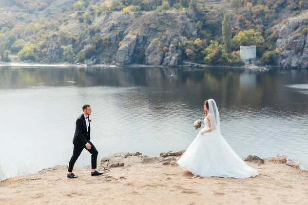 美しい豪華なカップルの結婚式の散歩 花束付きの結婚式の白いドレスの花嫁と自然の中で黒いスーツの新郎屋外 — ストック写真