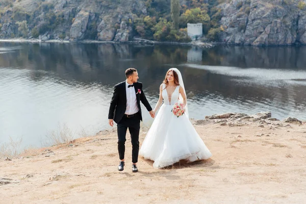 美しい豪華なカップルの結婚式の散歩 花束付きの結婚式の白いドレスの花嫁と自然の中で黒いスーツの新郎屋外 — ストック写真