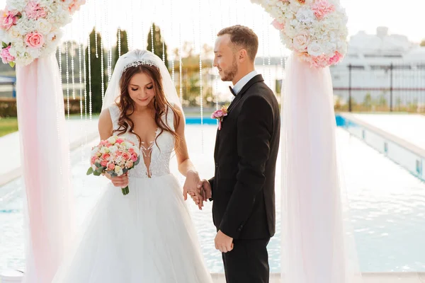 豪華な美しいカップル 黒いスーツの新郎と結婚式の白いドレスの花嫁は アーチ 秋の結婚式で終了式でリングを交換しました — ストック写真