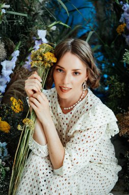 Güzel saç stili ve makyajlı, beyaz elbiseli, çiçekli, Vogue dergisi için moda tarzı bir odadaki kız model.