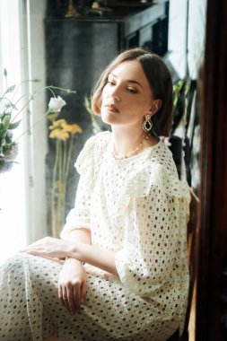 Güzel saç stili ve makyajlı, beyaz elbiseli, çiçekli, Vogue dergisi için moda tarzı bir odadaki kız model.