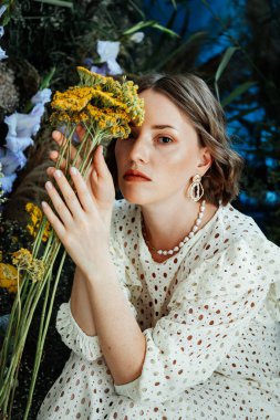 Güzel saç stili ve makyajlı, beyaz elbiseli, çiçekli, Vogue dergisi için moda tarzı bir odadaki kız model.