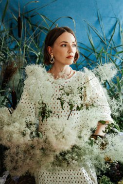 Güzel saç stili ve makyajlı, beyaz elbiseli, çiçekli, Vogue dergisi için moda tarzı bir odadaki kız model.