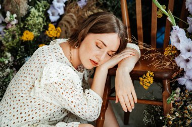 Güzel saç stili ve makyajlı, beyaz elbiseli, çiçekli, Vogue dergisi için moda tarzı bir odadaki kız model.