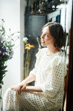 Güzel saç stili ve makyajlı, beyaz elbiseli, çiçekli, Vogue dergisi için moda tarzı bir odadaki kız model.