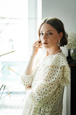 Güzel saç stili ve makyajlı, beyaz elbiseli, çiçekli, Vogue dergisi için moda tarzı bir odadaki kız model.