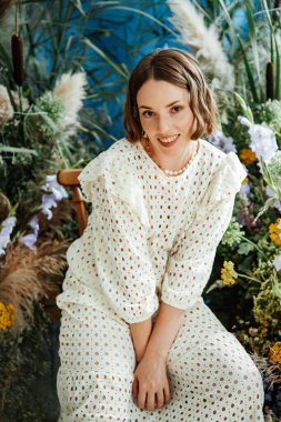 Güzel saç stili ve makyajlı, beyaz elbiseli, çiçekli, Vogue dergisi için moda tarzı bir odadaki kız model.