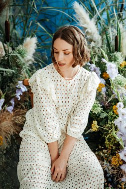 Güzel saç stili ve makyajlı, beyaz elbiseli, çiçekli, Vogue dergisi için moda tarzı bir odadaki kız model.