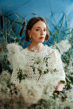 Güzel saç stili ve makyajlı, beyaz elbiseli, çiçekli, Vogue dergisi için moda tarzı bir odadaki kız model.