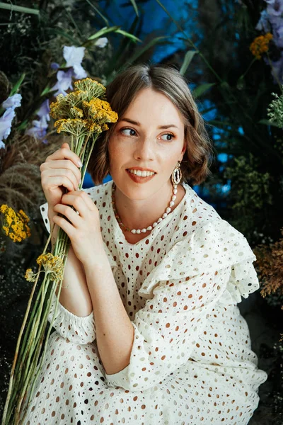 Güzel saç stili ve makyajlı, beyaz elbiseli, çiçekli, Vogue dergisi için moda tarzı bir odadaki kız model.