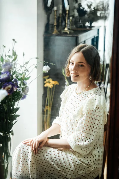 Güzel saç stili ve makyajlı, beyaz elbiseli, çiçekli, Vogue dergisi için moda tarzı bir odadaki kız model.