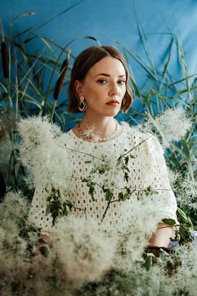 Güzel saç stili ve makyajlı, beyaz elbiseli, çiçekli, Vogue dergisi için moda tarzı bir odadaki kız model.