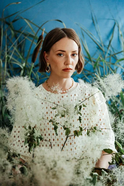 Güzel saç stili ve makyajlı, beyaz elbiseli, çiçekli, Vogue dergisi için moda tarzı bir odadaki kız model.