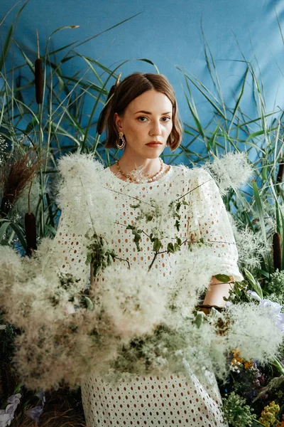 Güzel saç stili ve makyajlı, beyaz elbiseli, çiçekli, Vogue dergisi için moda tarzı bir odadaki kız model.