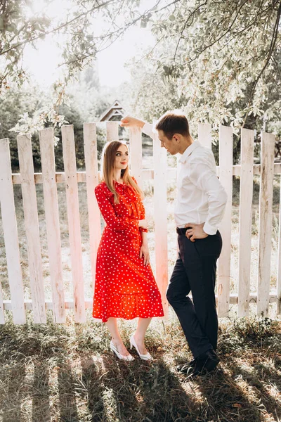 Beautiful couple, a girl in a red dress and a guy in a white shirt, are walking in the park in nature