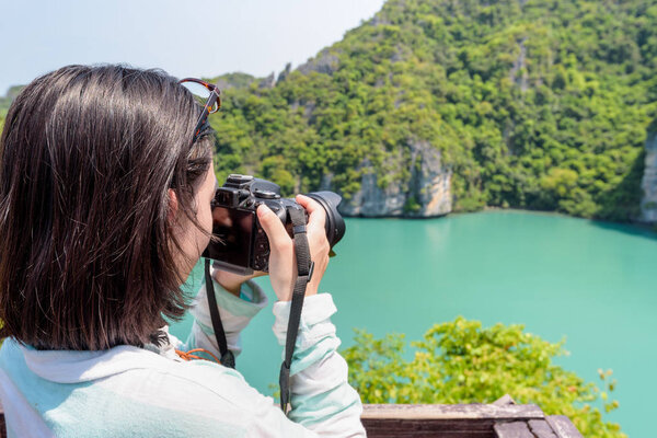 Woman tourist on Koh Mae Ko island viewpoint use camera taking photos at beautiful nature landscape of Thale Nai or Blue Lagoon (Emerald Lake) in Mu Ko Ang Thong National Park, Surat Thani, Thailand