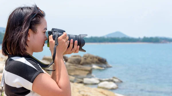 年轻女子高兴地拍摄与单反相机在海边的岩石上 在苏梅岛岛 素叻尼省 泰国的夏季天空 — 图库照片