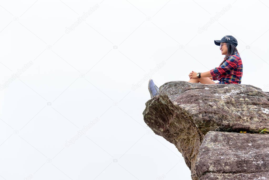 Asian woman sitting on a rock near a cliff on a white fog background looking forward with a happy smile.