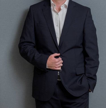 Elleri ceplerinde gri bir duvara olan akıllı takım elbiseli kırpılmış kafa adam ayakta