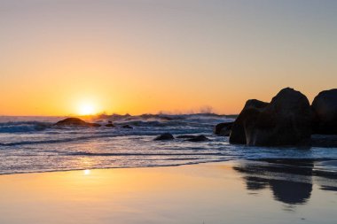 Plaj Cape Town Güney Afrika için karşı karşıya bir Batı kıyısında fotoğraflandı. Gün batımında kaba dalgalar su üzerine düşünceler ile kumlu bir plaj üzerinde