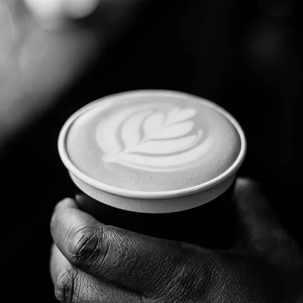 African Coffee Barista holding a take away cup with milk foam in a leaf shape