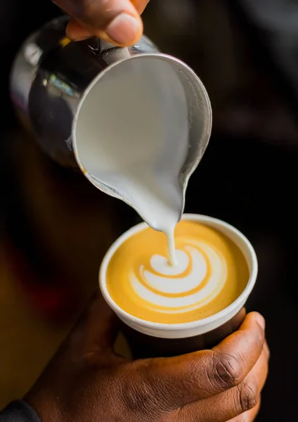 African Coffee Barista pouring a leaf shape with milk foam in a take away cup