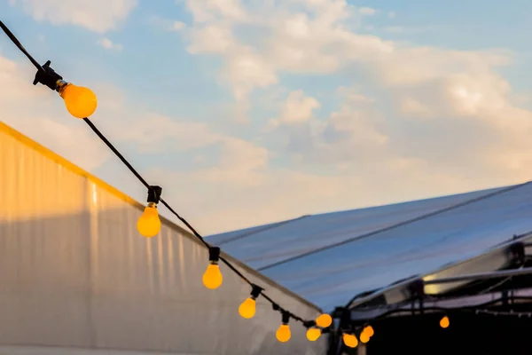 Light bulbs on a string hanging outside at party event with tents