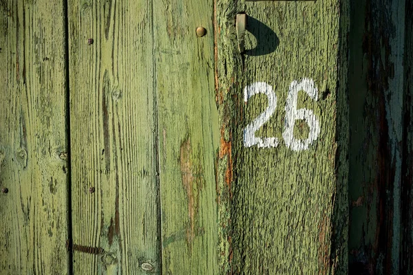 Number 26 with white paint on old green painted wooden door of the old house, a fragment of the facade. The picture was taken in Bulgaria in 2018