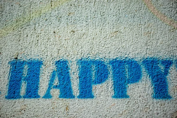 Happy blue paint word graffiti spray painted with template on white wall, close up