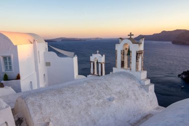 Kilise çatısının beyaz, haçlar ve Santorini, Yunanistan'ın çan. Derin deniz kristal suları ile arka planda caldera doğru şaşırtıcı gündüz gün batımı görünümü