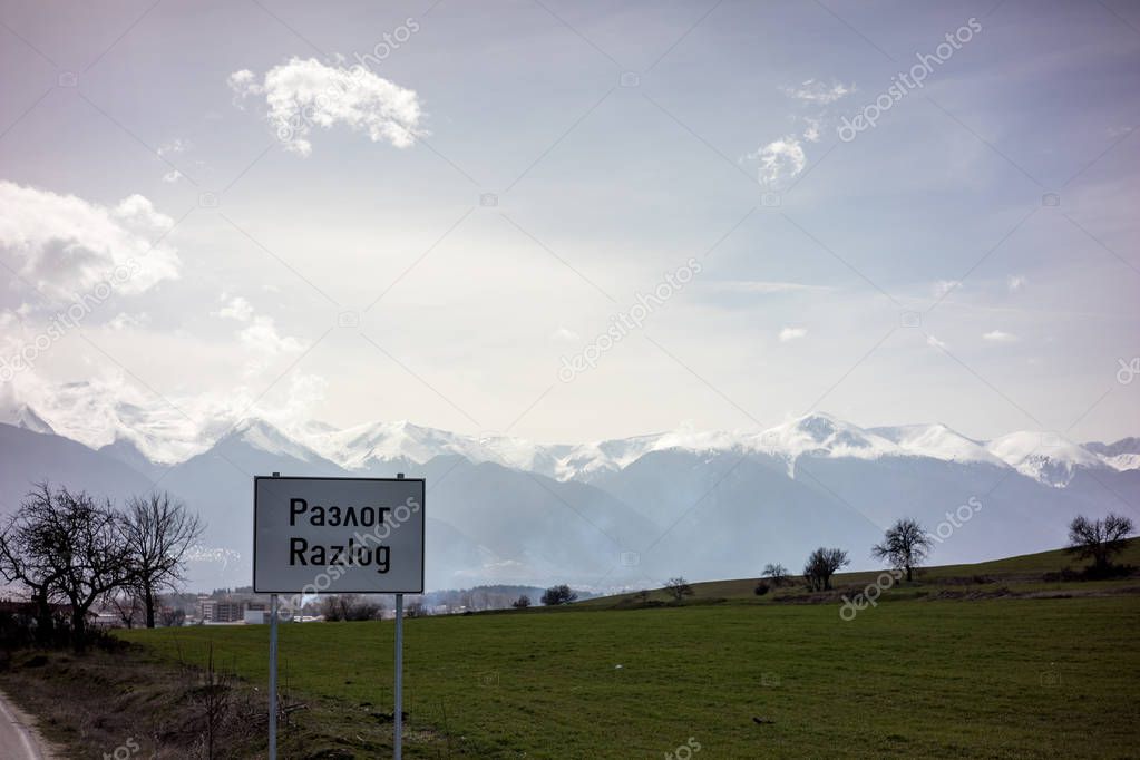 Moody springtime landscape at the entrance of Razlog, Bulgaria with the town sign. One could see the top of the Pirin mountain with Todorka and Vihren peaks.