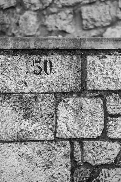 The number 50, house postal sign, painted with black paint, black and white image, stone wall, the digits are in the upper left-hand corner. Shot in Dubrovnik, Croatia
