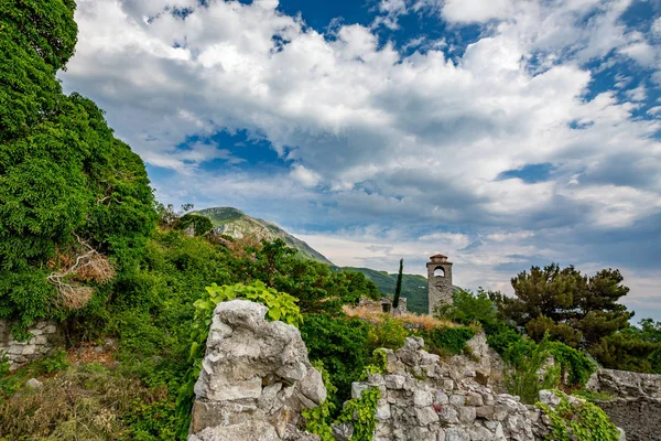 Springtime landscape of the ruins of Stari Bar ancient fortress, walking on arch way to ruined defense tower, in the medieval town of Bar in Montenegro. Renovated clock tower.