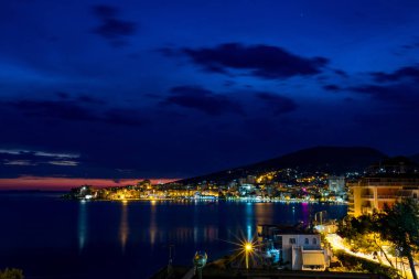 Uzun pozlama gece manzara fotoğraf, güzel deniz şehir Saranda, şehir ışıkları ve deniz yıldız efekti ile Arnavutluk, cityscape yansımaları su