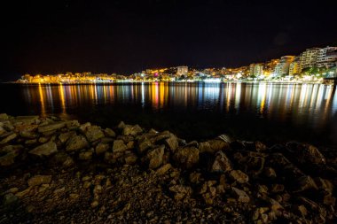 Uzun pozlama gece manzara fotoğraf, güzel deniz şehir Saranda, şehir ışıkları ve deniz yıldız efekti ile Arnavutluk, cityscape yansımaları su