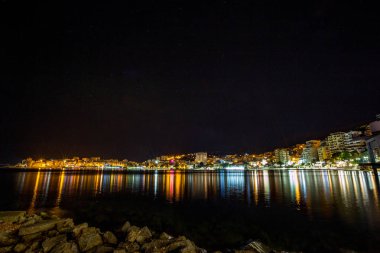 Uzun pozlama gece manzara fotoğraf, güzel deniz şehir Saranda, şehir ışıkları ve deniz yıldız efekti ile Arnavutluk, cityscape yansımaları su