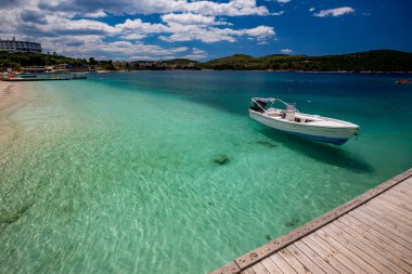 Gündüz güzel İyon Denizi berrak turkuaz su, ahşap iskele ve ince kum sahil manzaralı Ksamil plaj, Arnavutluk bahar. Derin mavi gökyüzü beyaz bulutlar ile.